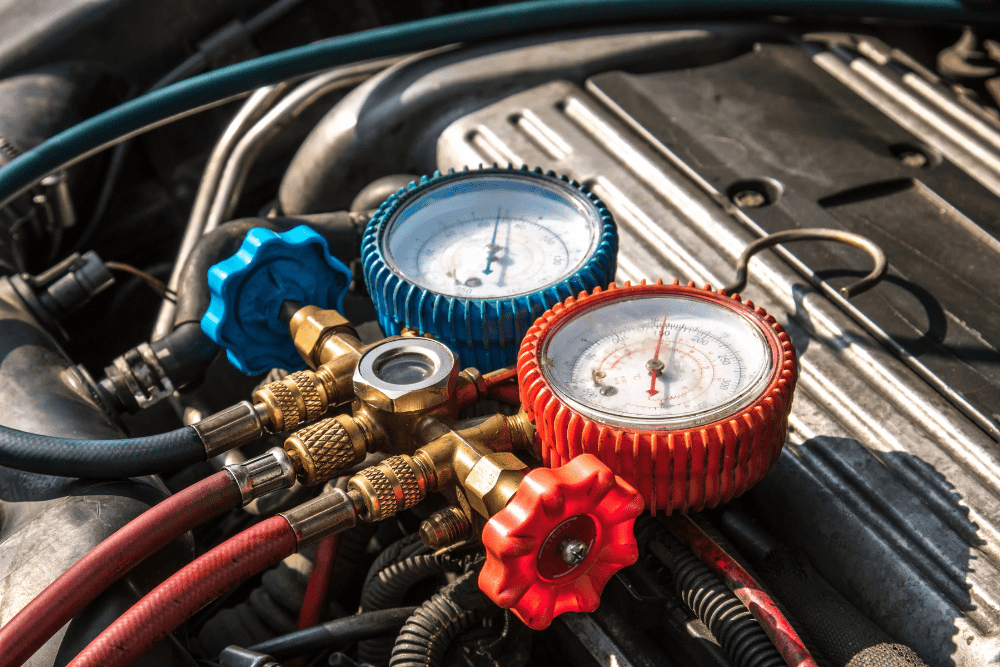 Car A/C Service in North Little Rock, AR by Cantrell Service Center. Image shows a close-up of red and blue manifold gauge set connected to a vehicle engine, highlighting accurate pressure testing for summer air conditioning service.