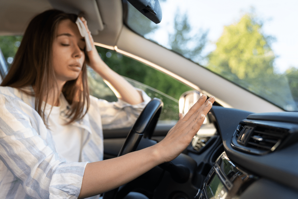 Car a/c blowing warm air, auto repair in North Little Rock, AR at Cantrell Service Center. Image of a woman driver struggling with heat inside the vehicle, highlighting the importance of reliable car A/C performance and cooling system service.